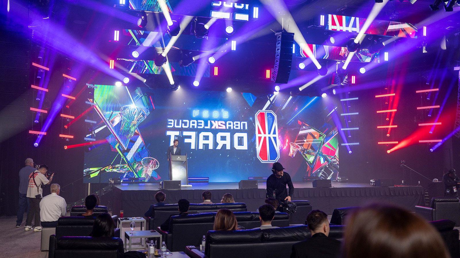 NBA 2 k联盟首席执行官安德鲁·珀尔马特站在舞台前的大屏幕上，屏幕上有NBA 2 k联盟选秀大会的标志.