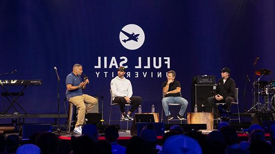 美国职业棒球大联盟投手亚当·温赖特和其他三个人坐在一个小组讨论的舞台上, 他们身后的大型LED屏幕在蓝色背景下写着“满帆大学”.